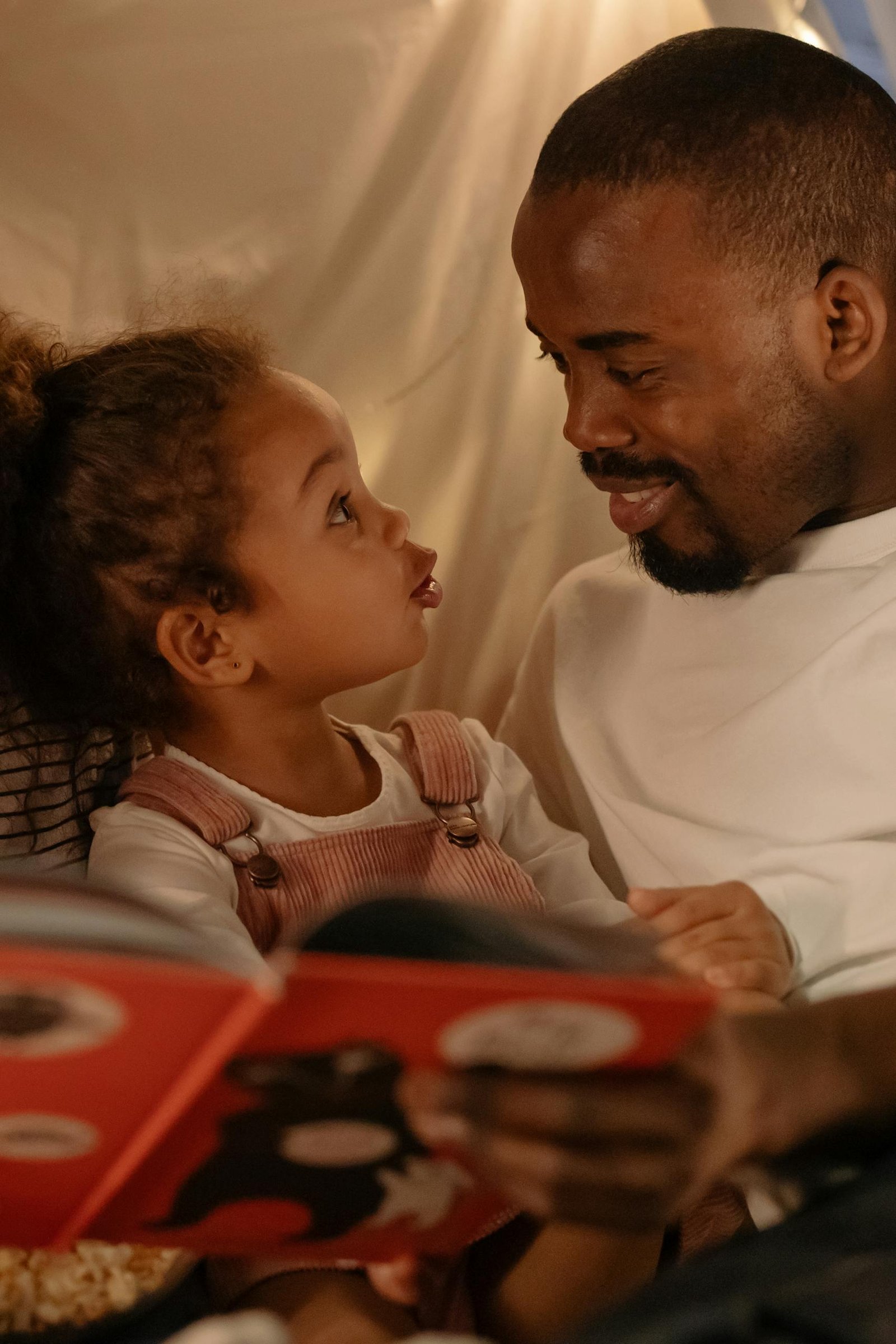 Father and daughter share a bonding moment reading a storybook indoors.