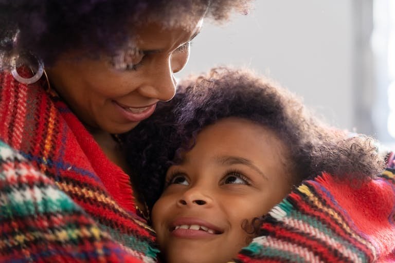 A joyful mother and daughter share an affectionate embrace wrapped in a colorful blanket.