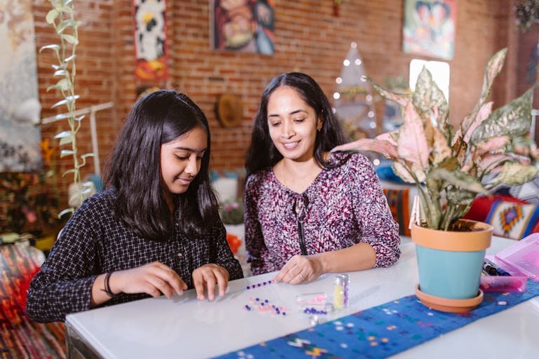 Mother and daughter creating a colorful beaded bracelet together at home.
