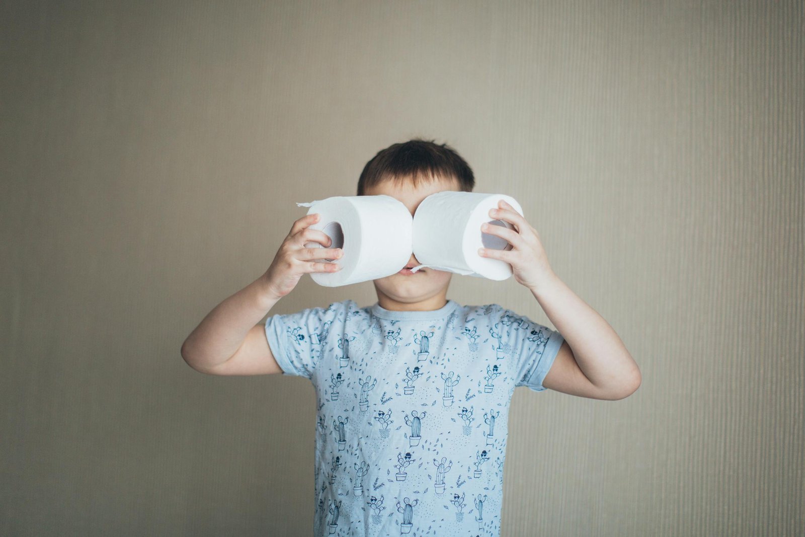 A young boy indoors, playfully using toilet rolls as binoculars, embodying fun and creativity.